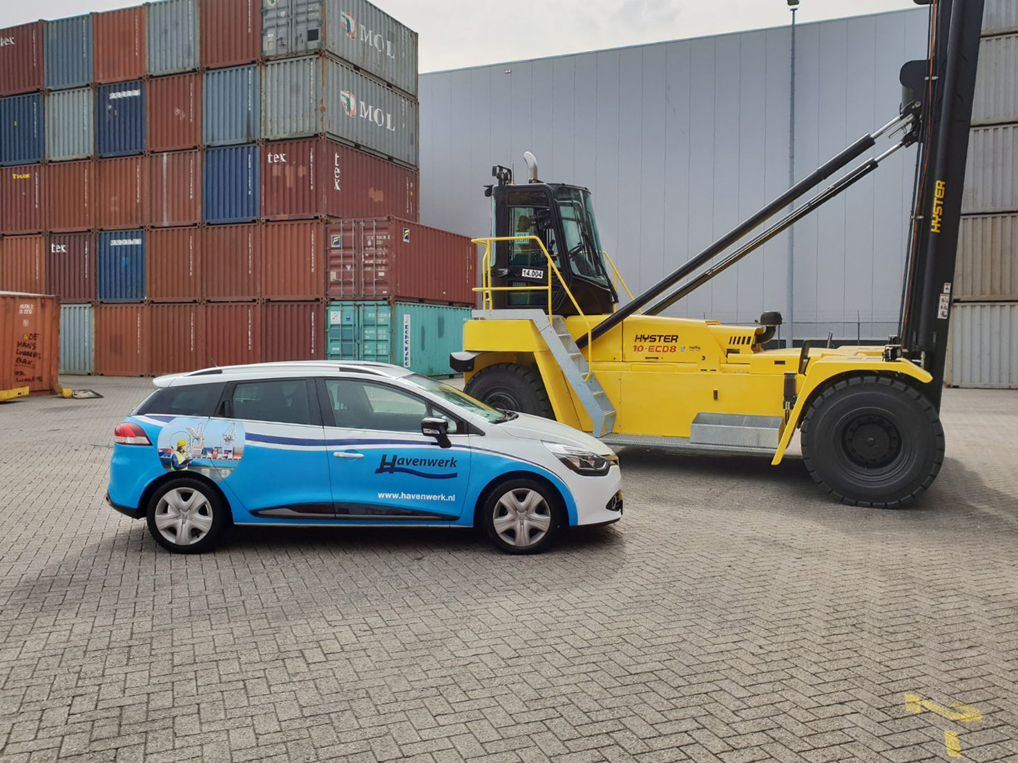 Bedrijfsauto van Havenwerk naast een reachstacker op een containerterminal